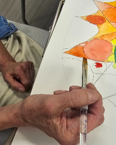 hand holding a paint brush in front of a painting during art therapy