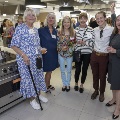 A group of smiling women in the kitchen filled with mingling people