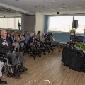 A room full of seated guests watch the program with a woman speaking on stage
