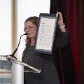 A woman speaks at a podium holding up an award