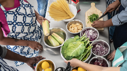 people cooking together at teaching kitchen event with fresh food such as corn, lettuce, onions, and whole grain pasta